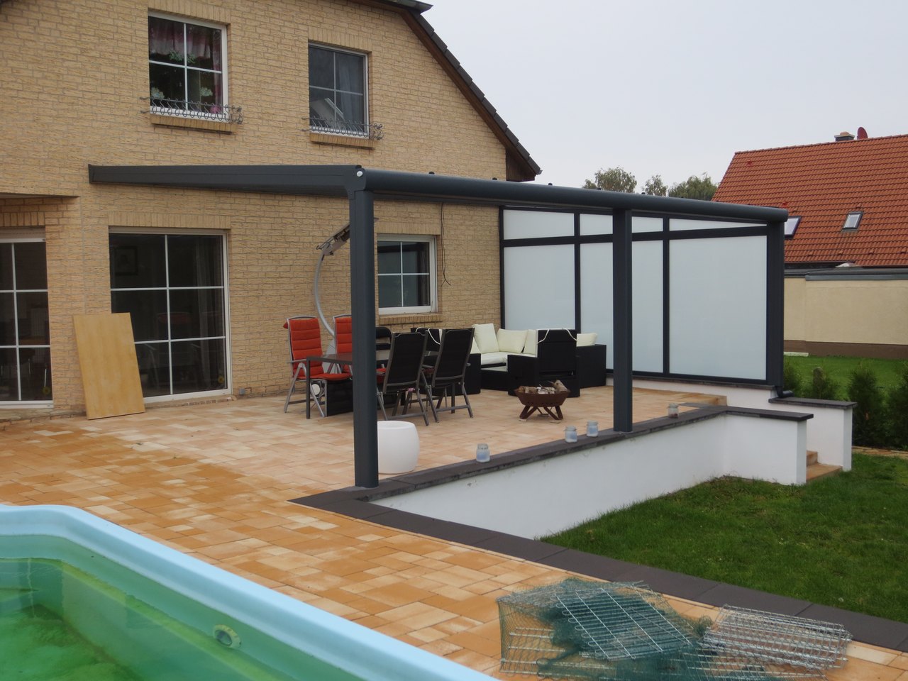 Moderne Terrasse mit grauer Überdachung, Außenmöbeln, Pool und angrenzendem Garten.