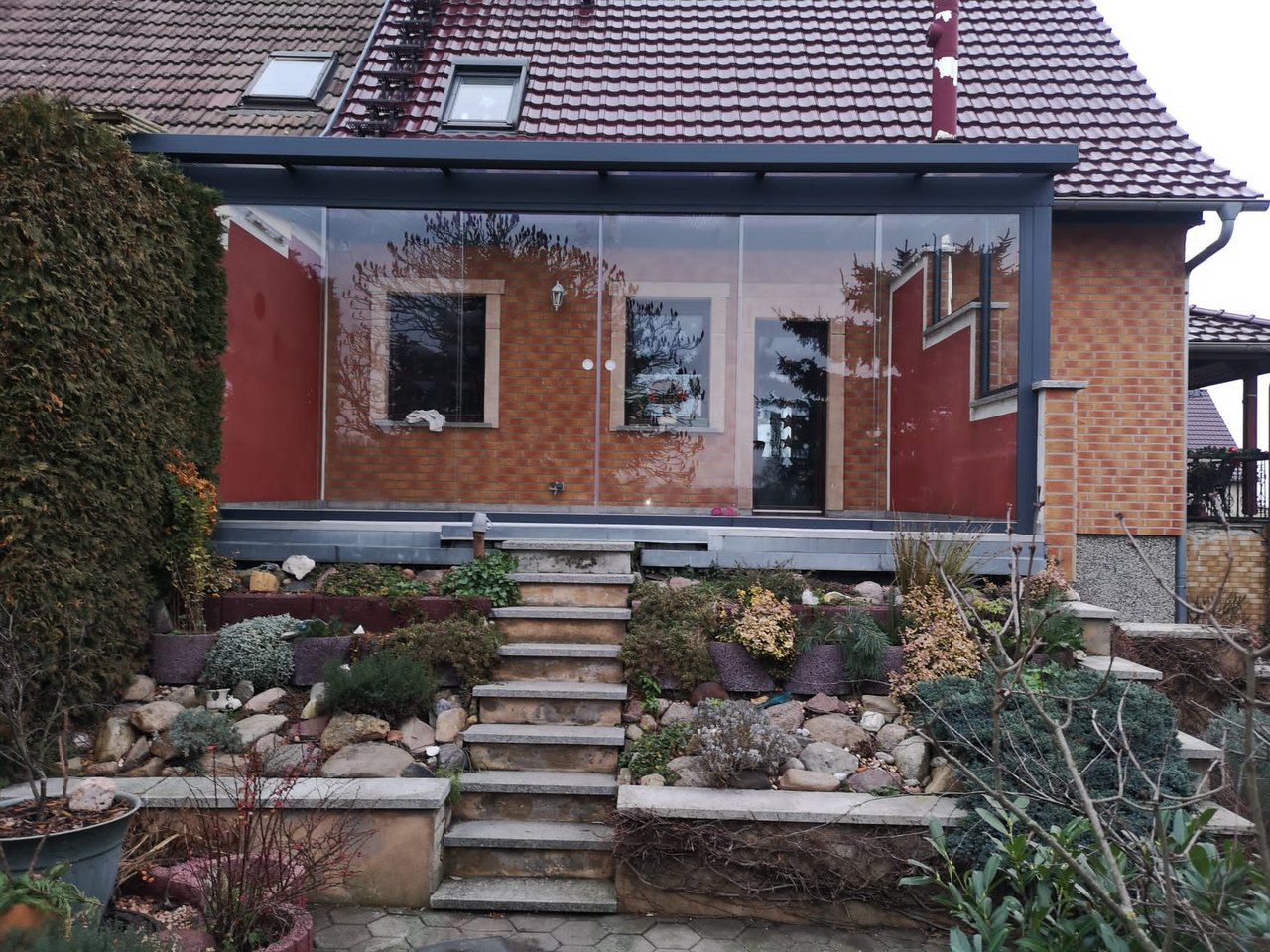 Eine Glasveranda mit Steinstufen und einem Gartenbeet davor.
